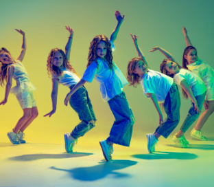 Happy children dancing. Group of children, little girls in sportive casual style clothes dancing in choreography class isolated on green background in yellow neon light. Concept of music, fashion, art