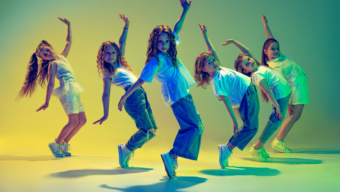 Happy children dancing. Group of children, little girls in sportive casual style clothes dancing in choreography class isolated on green background in yellow neon light. Concept of music, fashion, art